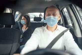 Taxi driver in a mask with a female client on the back seat wearing mask