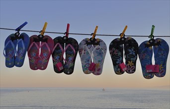 Bathing slippers hung on a line in front of the sea in the evening sun