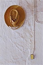 White wall with surface-mounted plug and power line and tattered straw hat