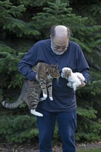 Elderly man holding cat and Bolonka Zwetna puppy in his arms