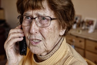 Senior citizen at home while phoning looks uncertain