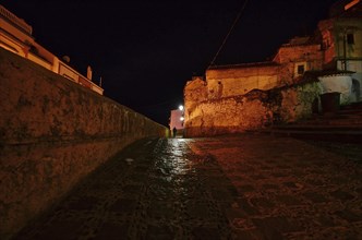 Sparsely lit alley with lone stroller at night on castle wall of Chefchaouen