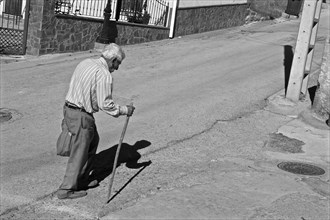 Bent old man with walking stick on street