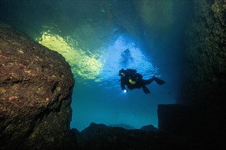 Diver swims diving through tunnel from inland sea of Gozo into passage to open sea