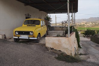 Yellow Renault R4 parked on terrace in front of house