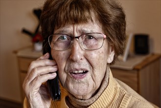 Senior citizen at home while phoning looks frightened