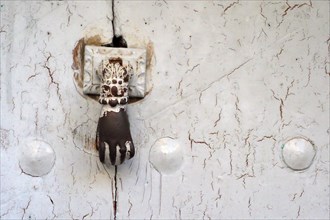 Iron door knocker as hand on white wooden door