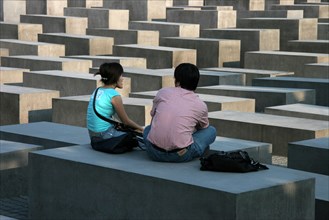 Asian woman and man sitting on concrete blocks from the Memorial of the Murdered Jews