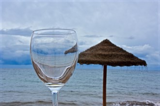 Empty wine glass in front of a sisal parasol by the sea