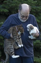 Elderly man holding cat and Bolonka Zwetna puppy in his arms