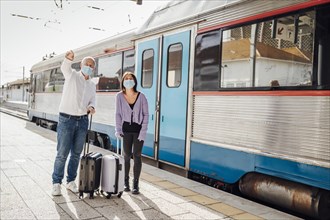 Tourists with suitcases and masks on the platform next to the train
