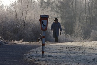 Male walker with dog in park with hoarfrost and emergency phone