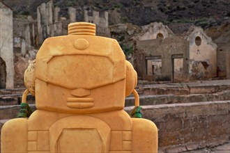 Head of a yellow plastic figure in front of ruins of a mine in Mazarron