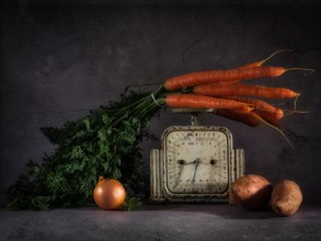Still life with carrots on old kitchen scales next to onions and sweet potatoes