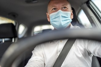 A man in a protective mask driving a car
