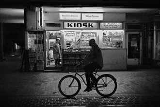 Man on bicycle in front of kiosk at night