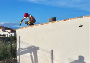 Bricklayer squats on house roof and grouts the roof tiles