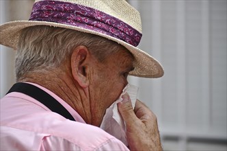 Old man with straw hat from the side blows his nose