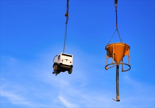 Construction machinery chained to a construction crane against a blue sky