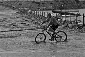 Man on bicycle on flooded bridge after heavy rain