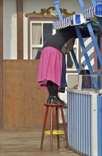 Woman in dirndl stands on stool and cleans