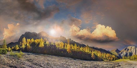 Glowing autumnal mountain forest below the Lamsenjoch massif with bizarre cloudy sky