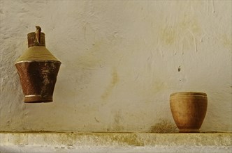 Oil can and clay jug in front of white wall in cave house