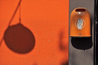 Orange waste bin with orange wall and shadow of a lamp