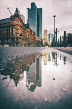 View of a street with old buildings and modern skyscrapers in the morning rain. Everything is reflected in a puddle. Bankenfirtel