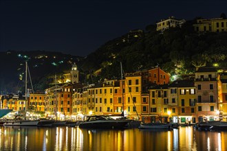 Boats anchor in Portofino harbour at night in front of illuminated pastel-coloured house facades
