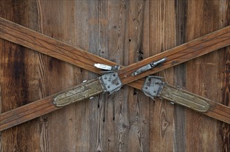 Crossed pair of old wooden skis on brown wooden wall