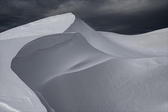 Snow cornice against a dark sky at the summit of Toreck