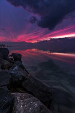 Magical sunset at a lake. Red and purple clouds reflected in the still water. After the sunset with stone shore in Siofok