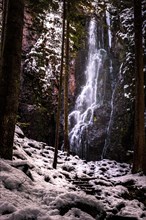 The Burgbach waterfall with snow in winter. Waterfall with stone steps in Schapbach