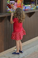 Girl in red dress in front of kiosk with sweets