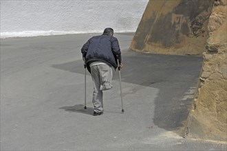 Disabled one-legged man on crutches walks in the street