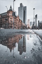 View of a street with old buildings and modern skyscrapers in the morning rain. Everything is reflected in a puddle. Bankenfirtel