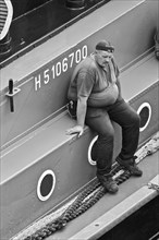 Potbellied sailor with cap sits pensively on ship