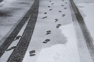 Black tracks from car tyres and footprints in the snow on asphalt road