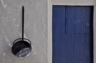 Long-handled pan on house wall with blue front door