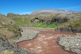 Reddish brown river flowing through a green arctic landscape