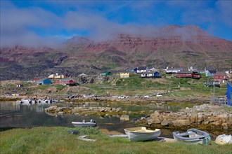 Small boats lie in front of houses and red volcanic mountains