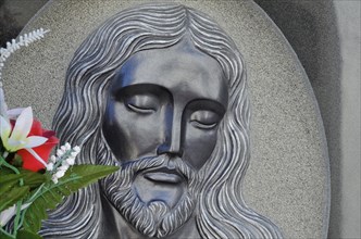 Head of Jesus on grave slab with artificial flowers