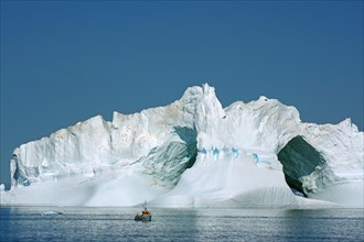 Small fishing boat in front of huge iceberg with two large caves