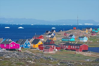 Different coloured wooden houses in front of the bay with icebergs