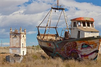 Painted wreck of fishing boat in front of old pigeon tower