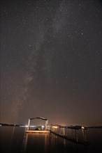 Night view of the Milky Way with illuminated jetty in the foreground