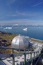 Igloo-shaped tourist accommodation on the edge of a bay covered in icebergs