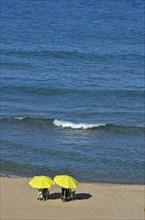 Beachgoers under yellow umbrellas by the sea with wave