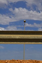Guard rail from behind with street lamp and cloudy blue sky